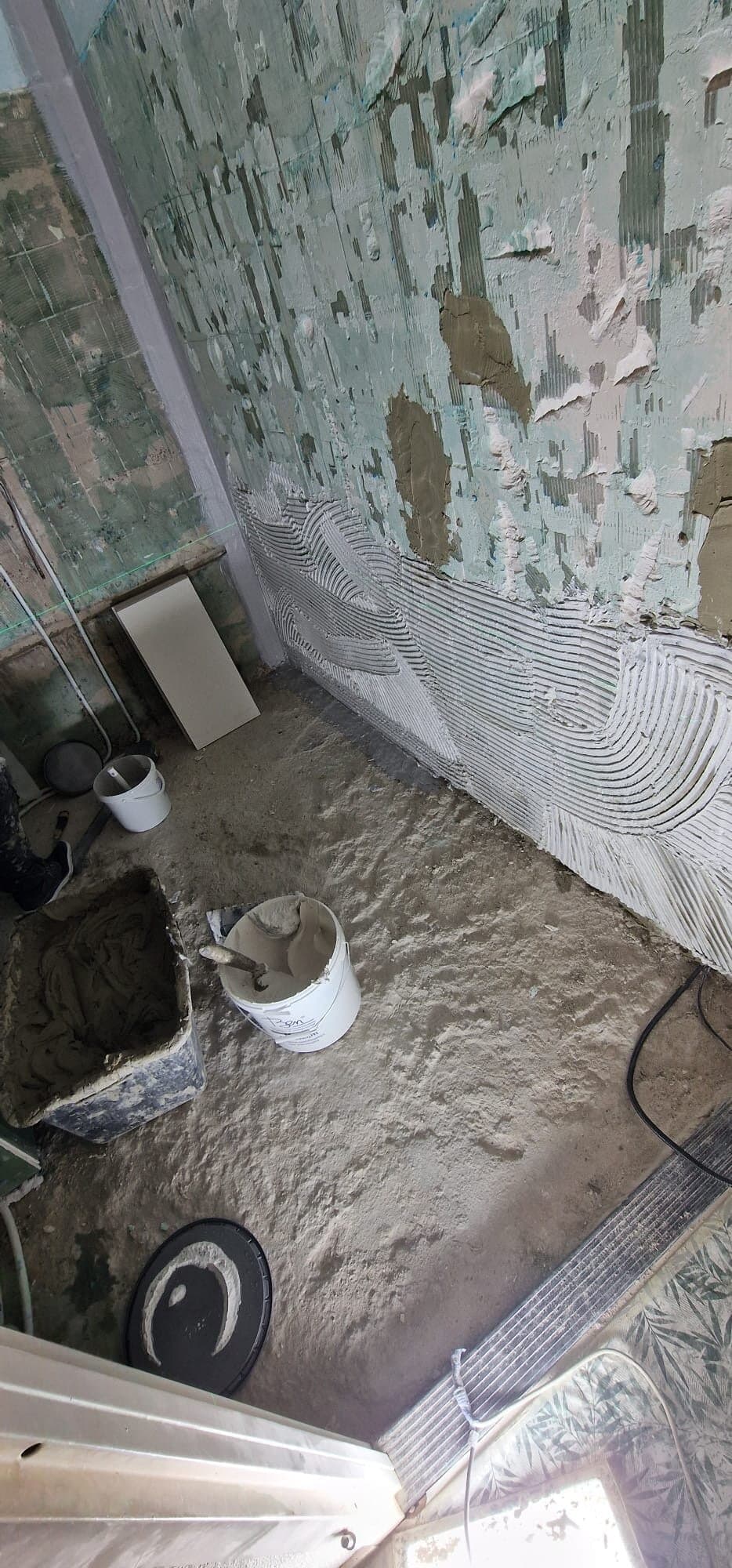 Gestripte badkamer met oude lijmresten en een vers gekamde lijmlaag op de wand
