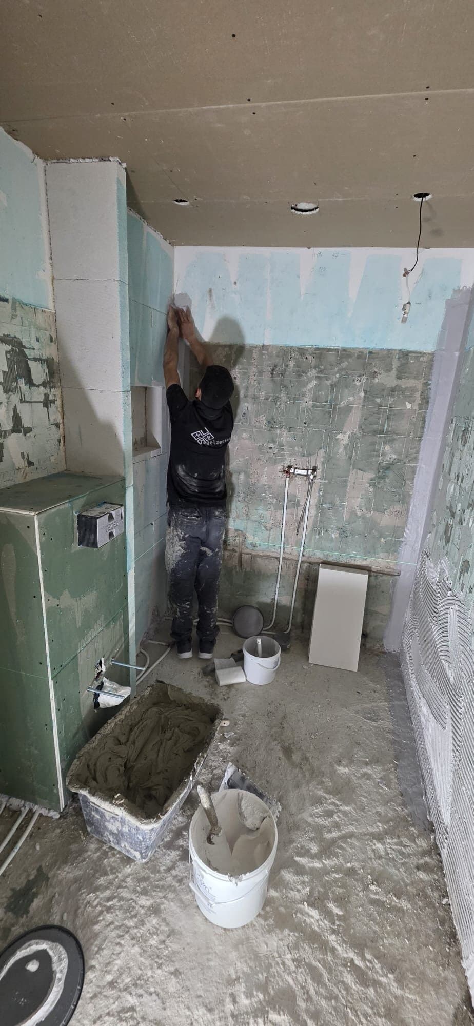 Tegelzetter aan het werk in een gestripte badkamer met voorzetwand voor het toilet