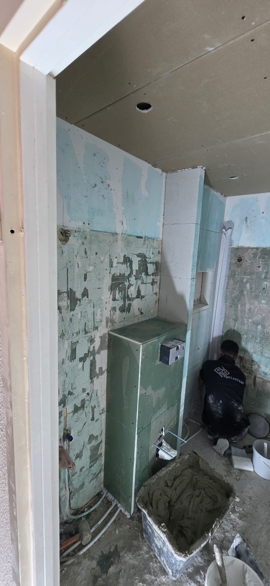 Tegelzetter aan het werk naast de voorzetwand in een badkamer in renovatie