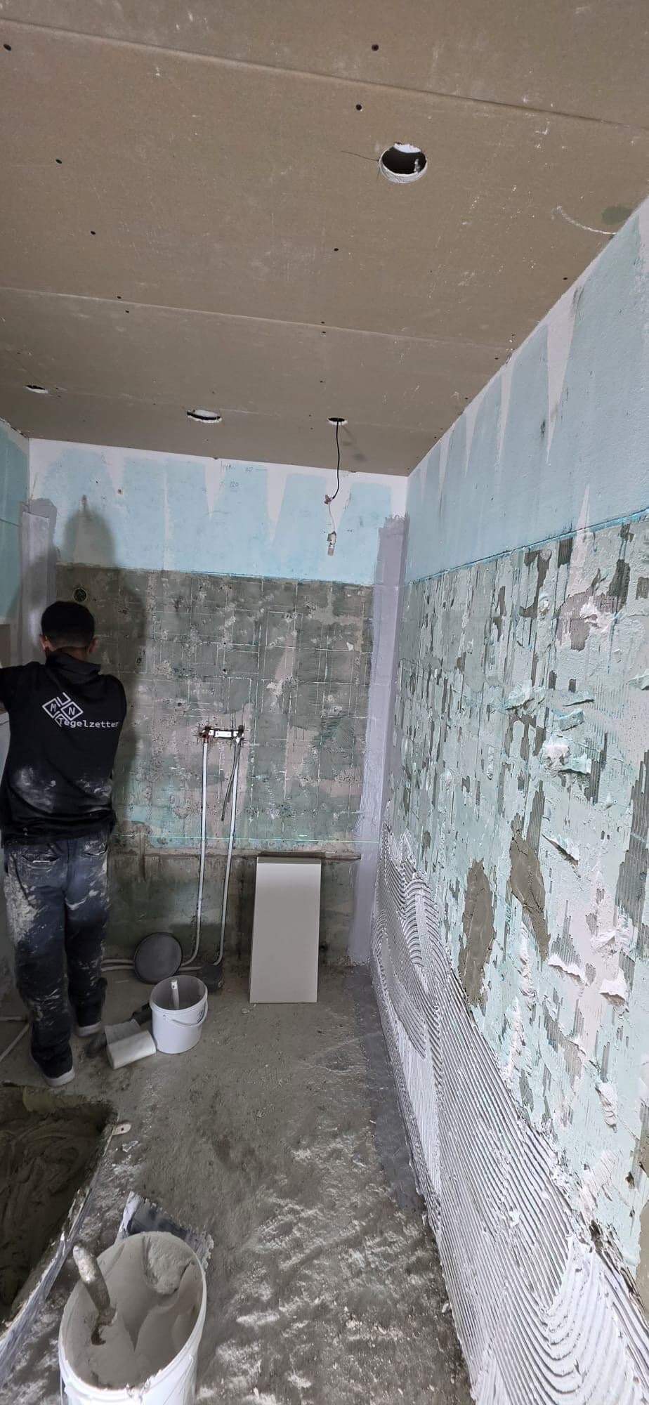 Tegelzetter aan het werk in een smalle badkamer tijdens het voorbereiden van de wanden