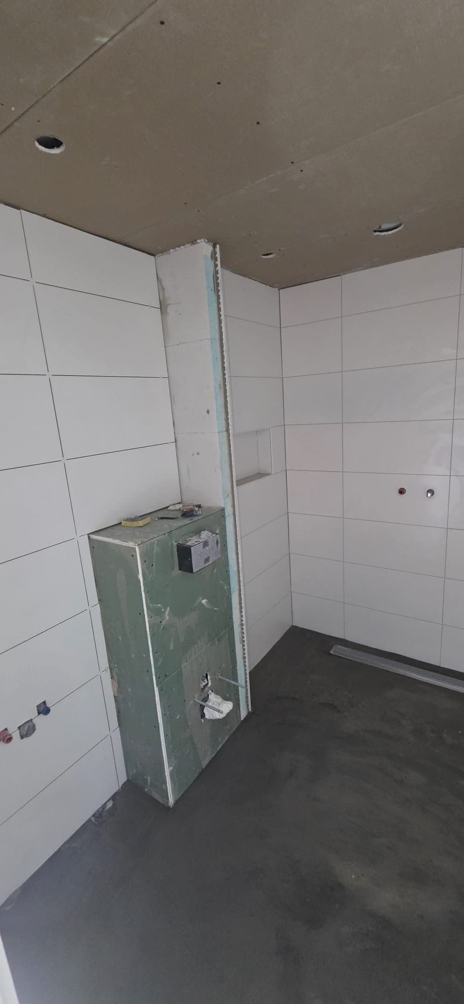 Badkamer met witte wandtegels en een voorzetwand voor het hangend toilet in aanbouw