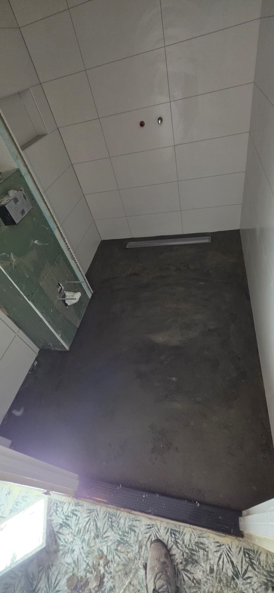 Badkamer met witte wandtegels en een vlakke douchegoot, de vloer nog in voorbereiding